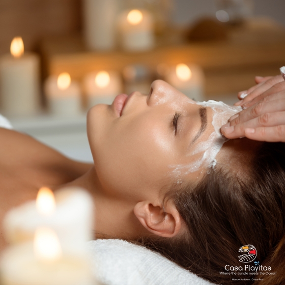 Woman receiving a facial treatment with a white cream mask on her forehead, in a candlelit spa setting.